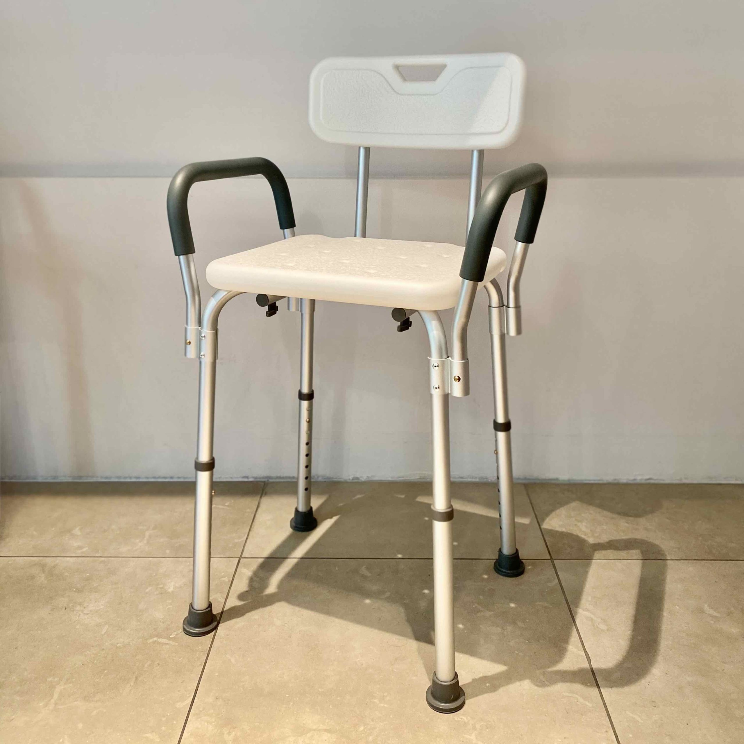 Sedia da doccia ortopedica in alluminio e polietilene bianco con schienale, braccioli imbottiti e puntali a ventosa.
