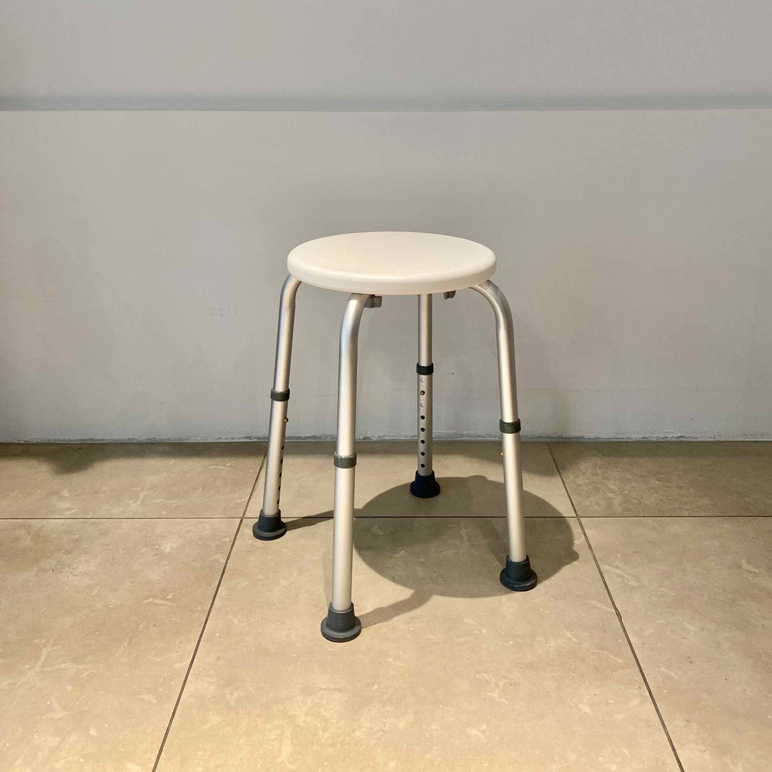 Sgabello tondo da doccia ortopedico in alluminio con seduta circolare bianca in plastica e gambe regolabili.
